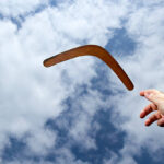 Lancer un boomerang en bois ordinaire dans les airs avec un ciel bleu et un fond de nuage