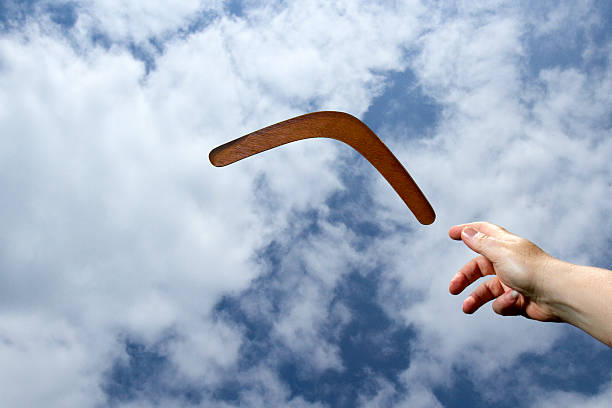 Lancer un boomerang en bois ordinaire dans les airs avec un ciel bleu et un fond de nuage